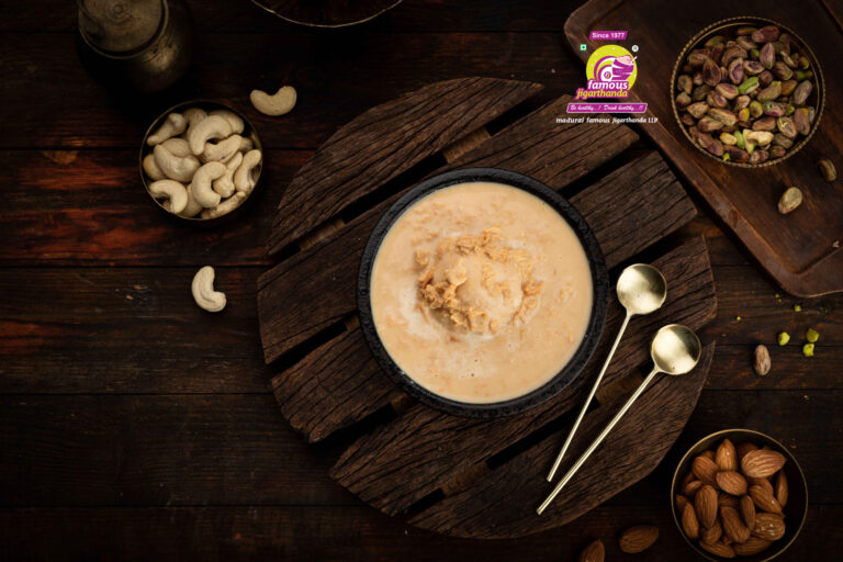 A bowl of Basundi with toppings, surrounded by cashews, pistachios, almonds.